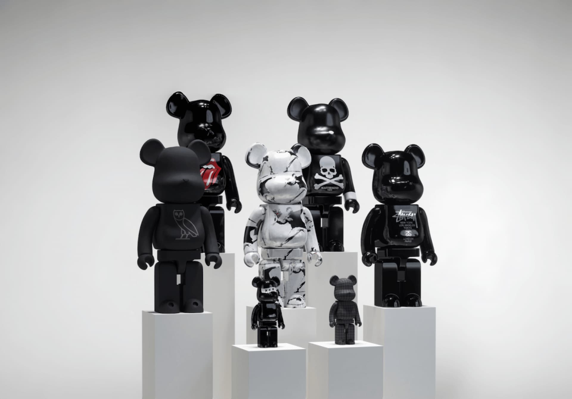 Category side 1000% Bearbricks new Stylized display of 1000% Bearbrick figures in sleek black and marble designs, including brands like Stussy and Mastermind, showcased on minimalist white podiums.