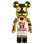Discover the Hottest Basketball Bearbricks Front view of 1000% Bearbrick Michael Jordan 1991 World Champion edition figure, featuring a gold reflective head and arms, white Chicago Bulls jersey with “BULLS” and number 23 in red, NBA logo, black armband, and basketball court-themed legs with red Jumpman logo on sneakers.