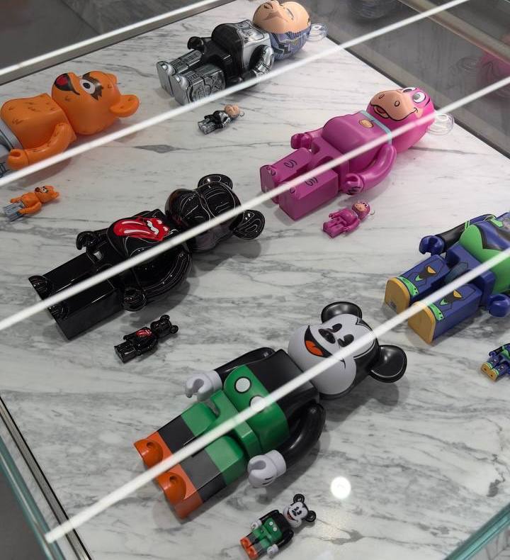 Bearbrick figures of various sizes and characters displayed on a marble surface under glass.